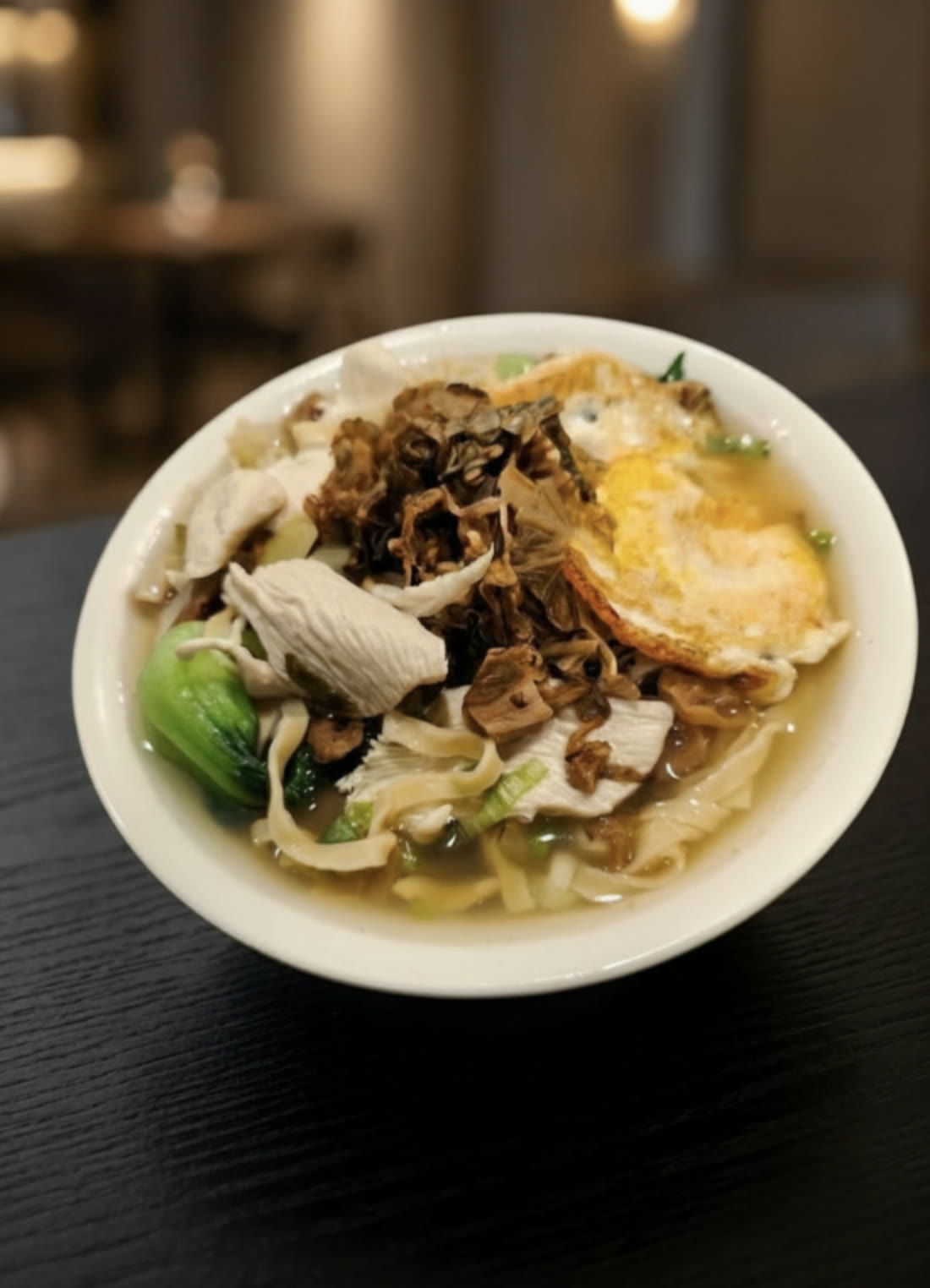 You Yi’s preserved mustard greens noodle soup with sliced chicken, fried egg, and bok choy — styled presentation of the restaurant’s dish.