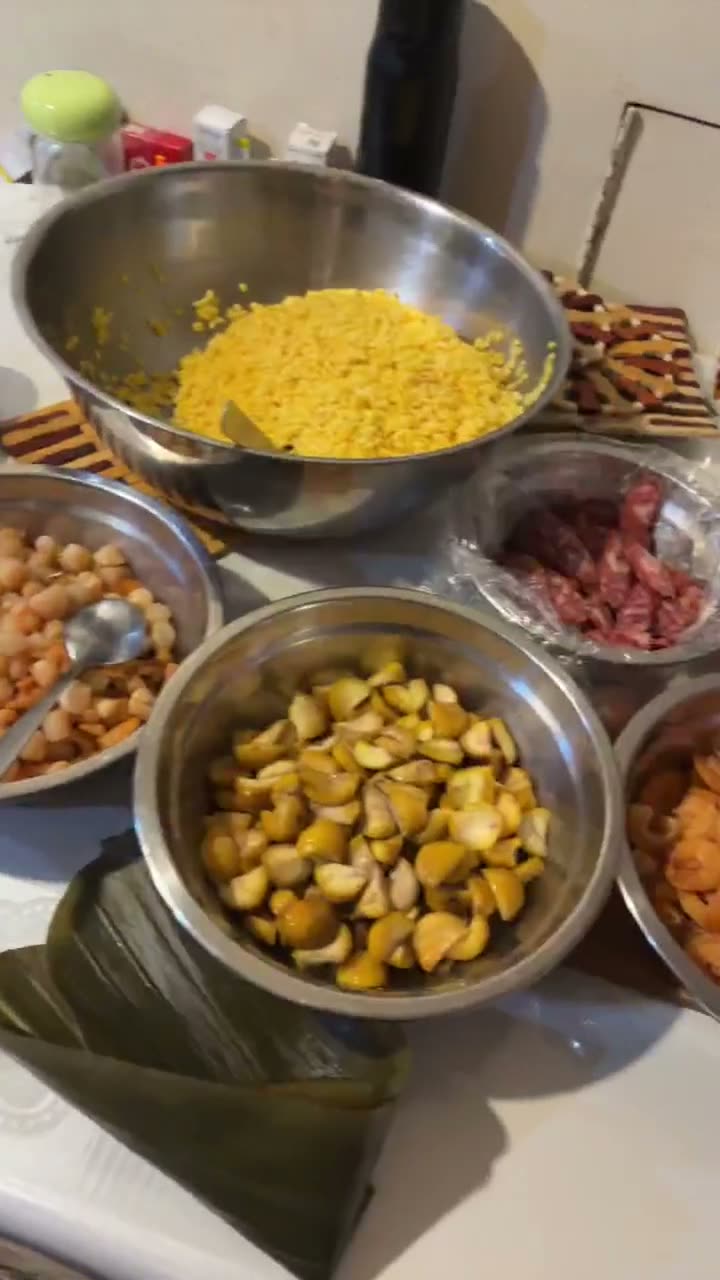 Video of the raw ingredients for You Yi’s sticky rice dumplings — bowls of glutinous rice mixed with mung bean, chopped chestnuts, dried shrimp, and marinated pork, with a bamboo leaf ready for wrapping.